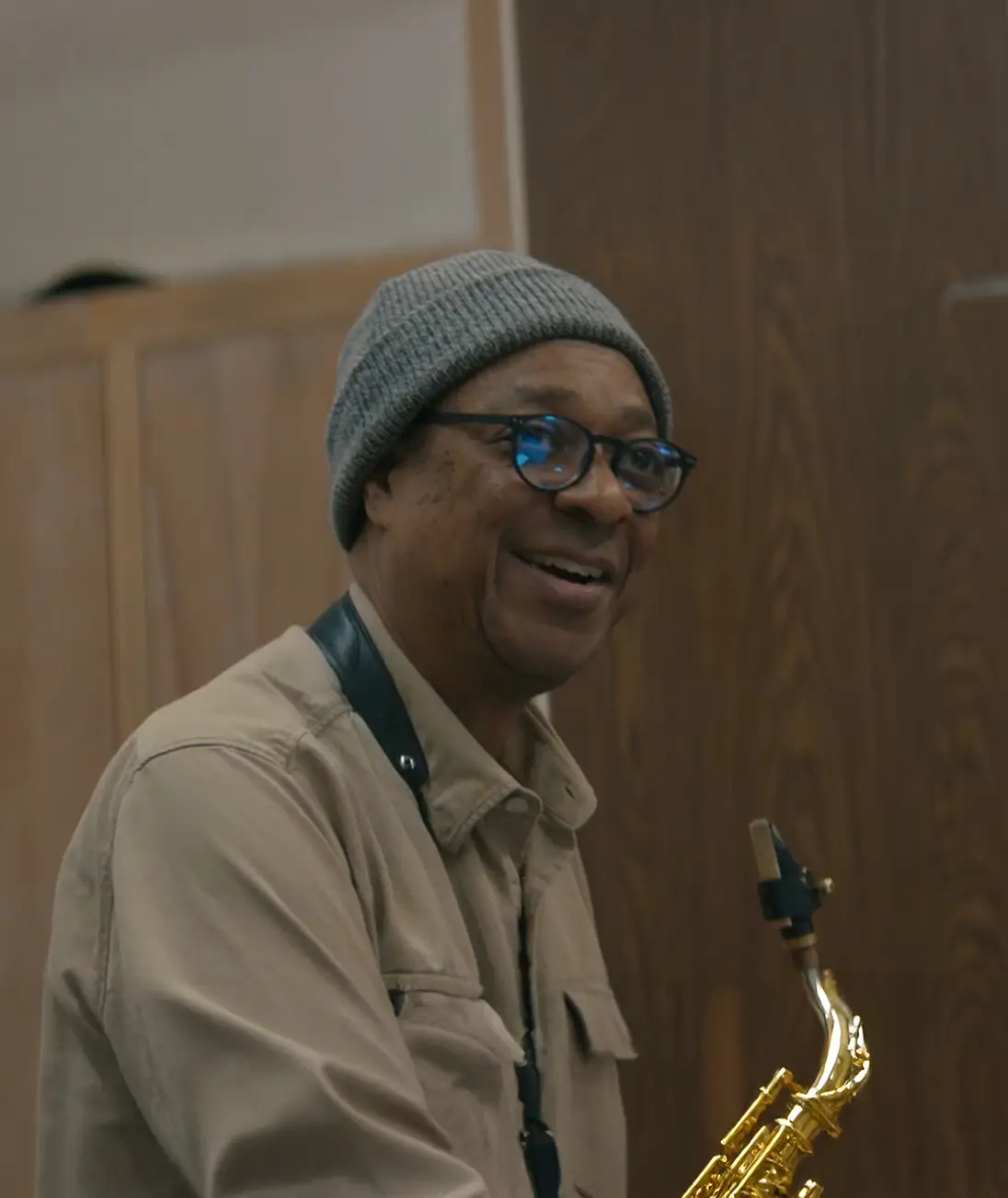 Man smiling while holding a saxophone indoors