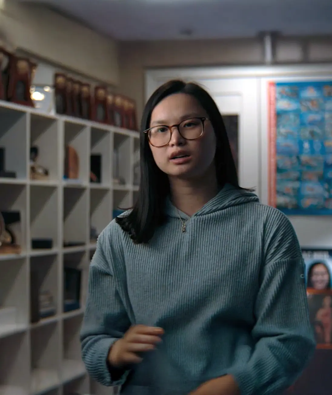 Woman in glasses speaking in front of display shelves and framed items