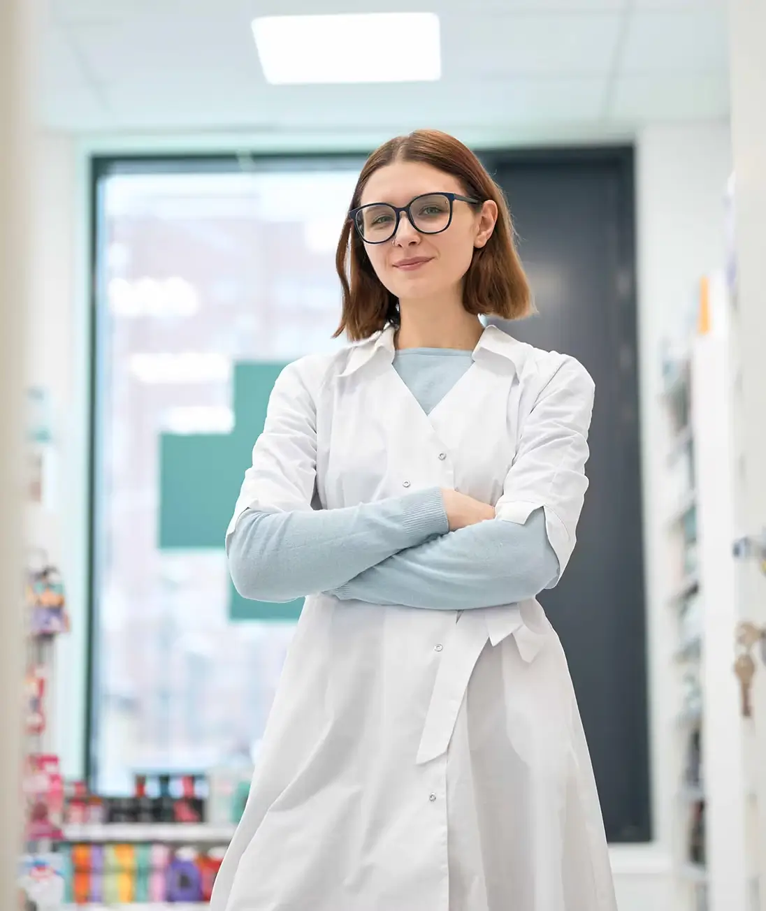 Young woman in white robe and glasses crossing arms and looking at camera with smile