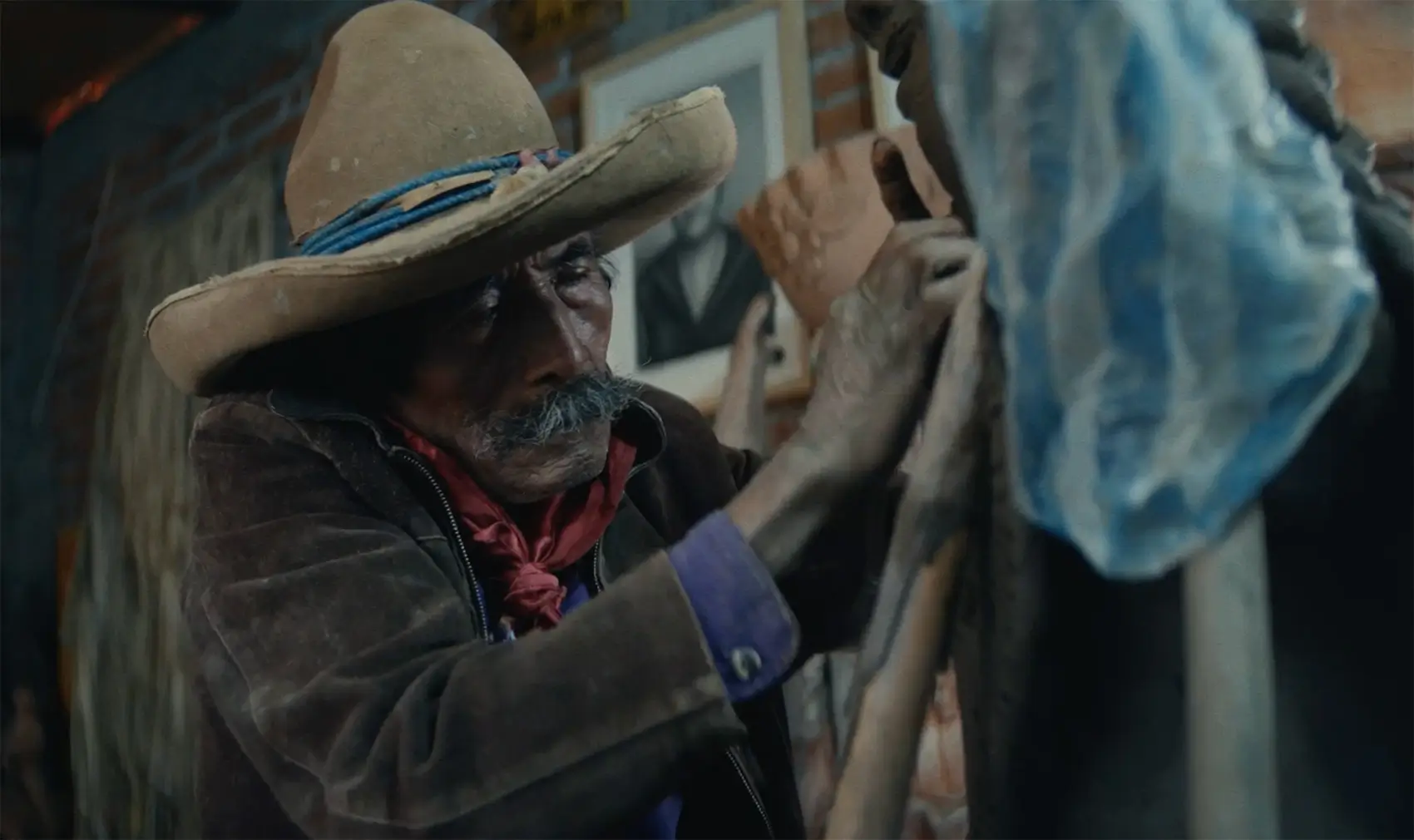 An elderly man in a hat carefully working on a clay sculpture