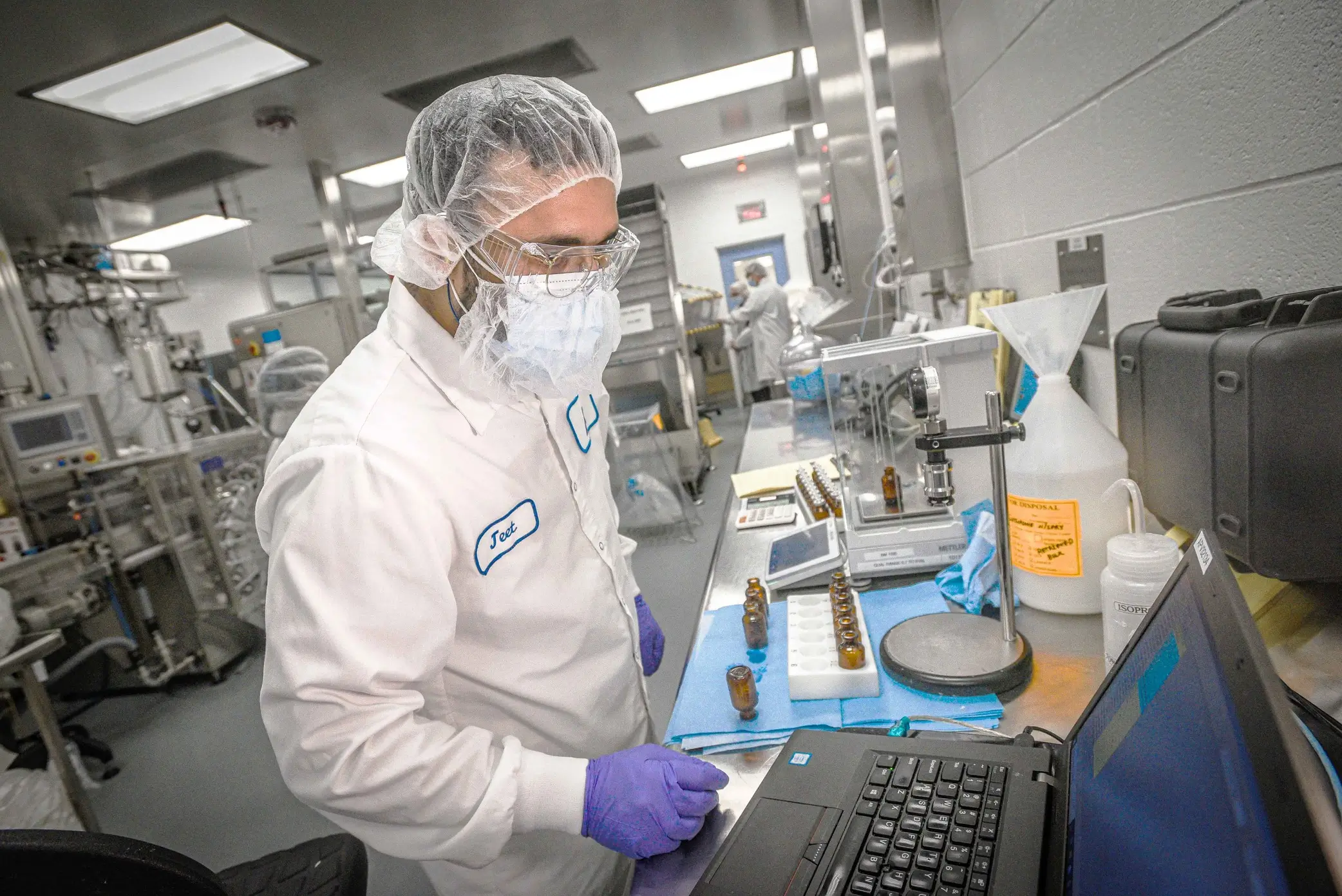 A scientist working with vials and a laptop in a laboratory