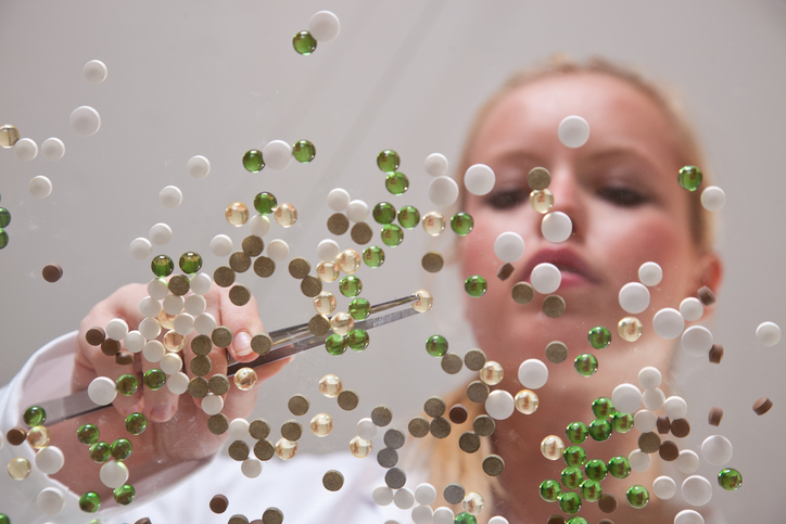 A person using tweezers to manipulate small, colorful spheres