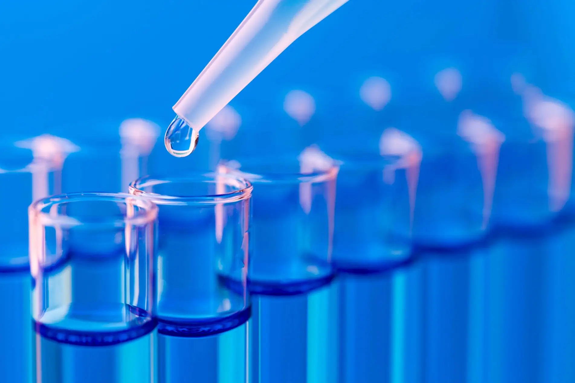 A macro shot shows a single drop of clear liquid falling from a pipette into a test tube