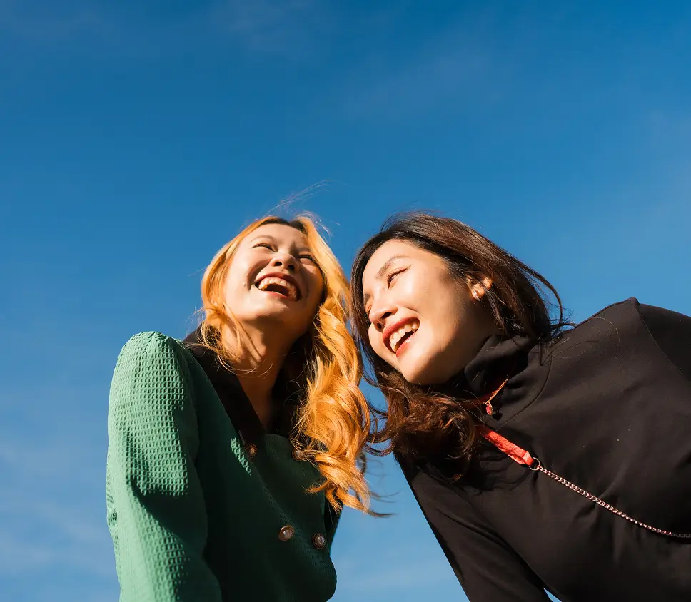 Two young women smiling and looking up toward the clear blue sky.