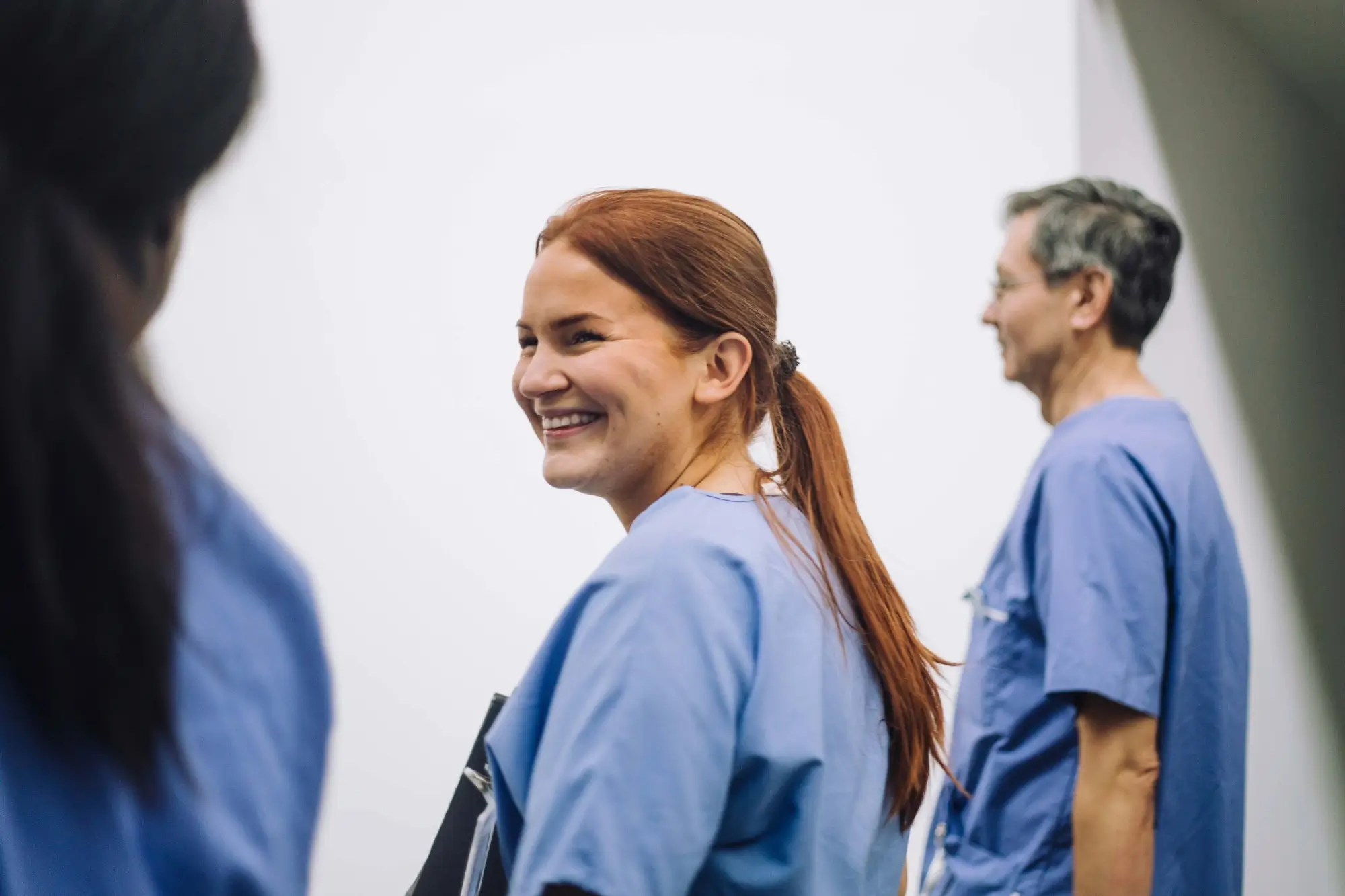 A woman in blue scrubs smiles while standing with two colleagues