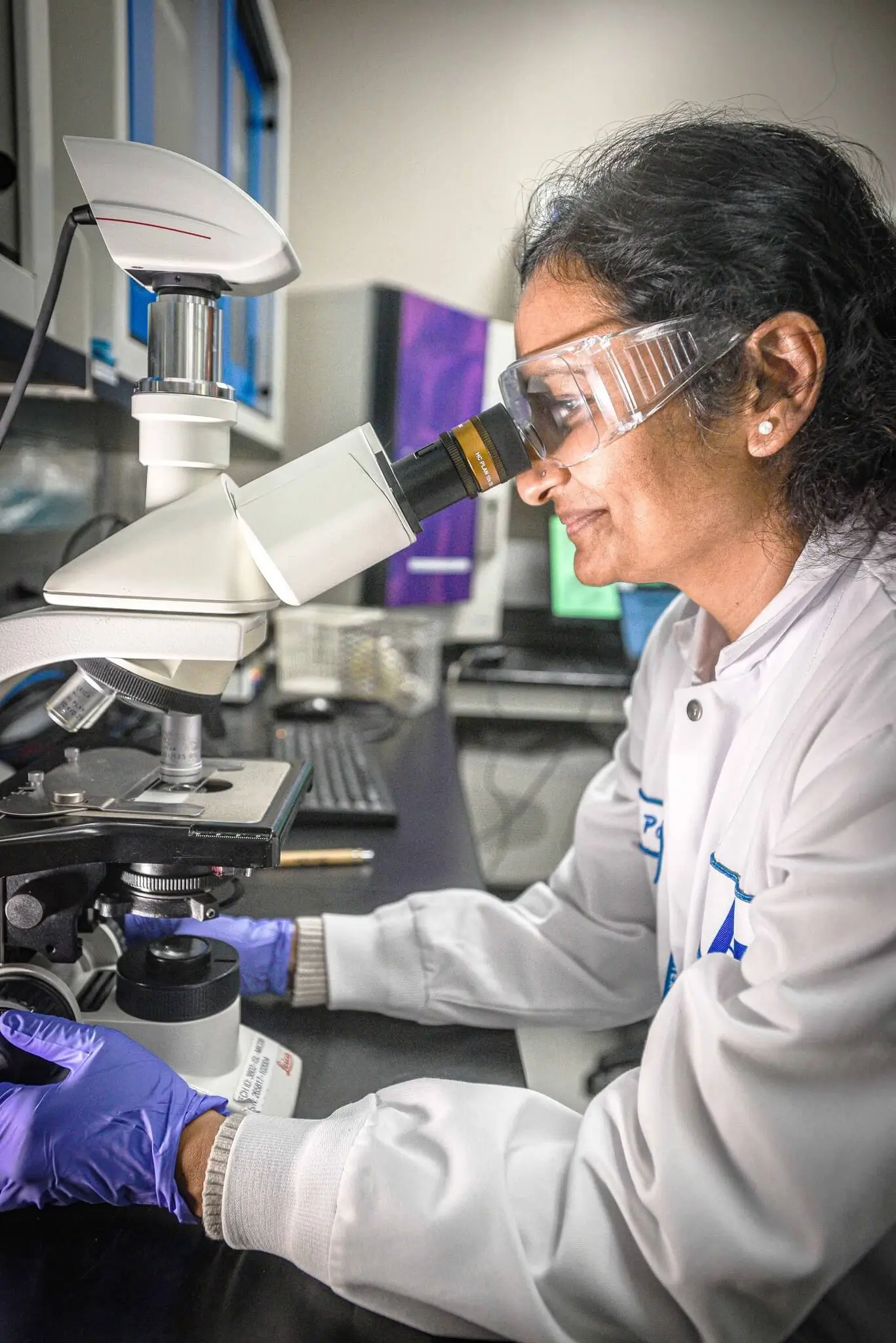 A scientist in a lab coat and safety goggles using a microscope