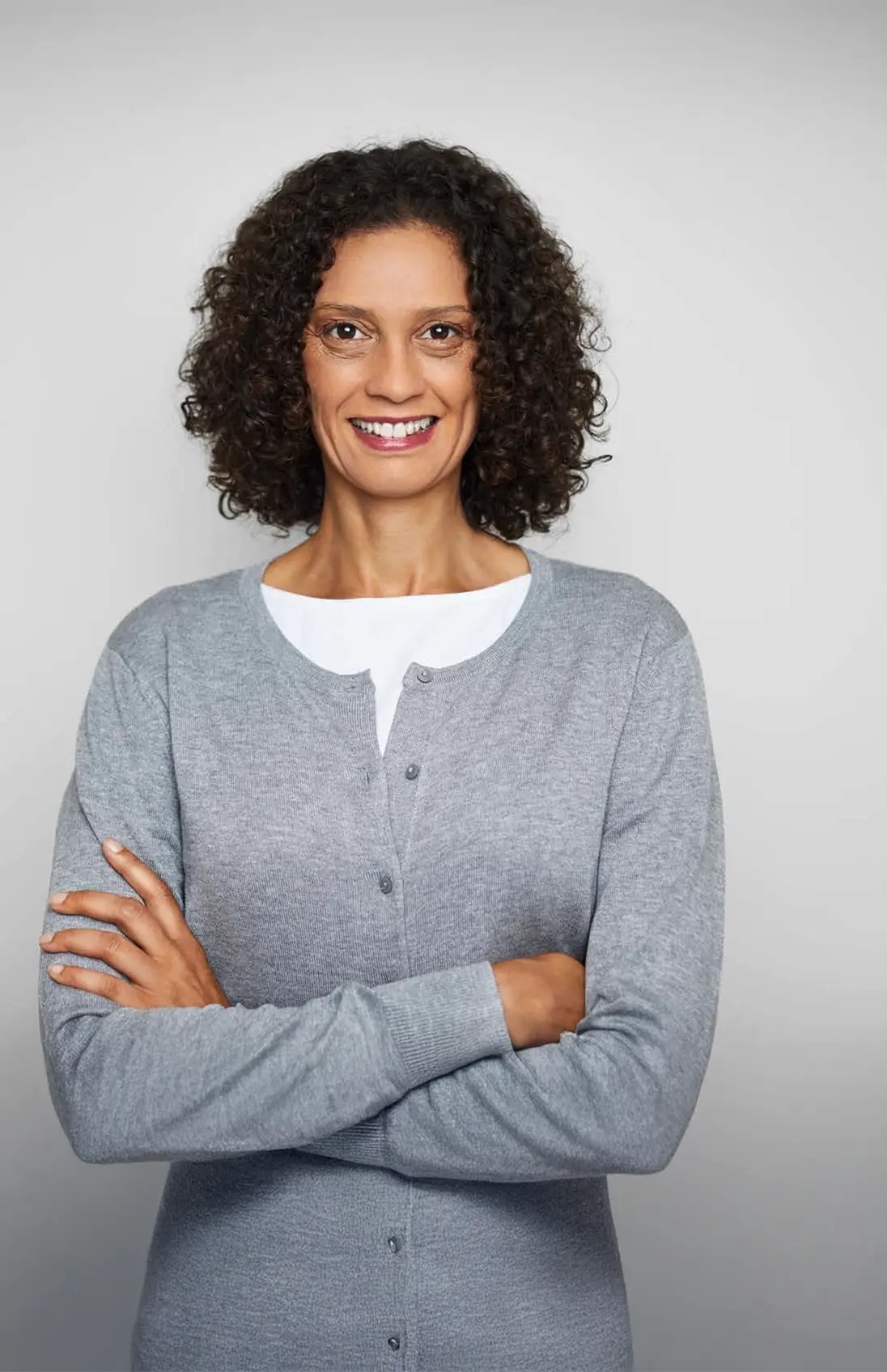 Une photo d’une femme d’âge moyen, les bras croisés, souriante et regardant droit devant