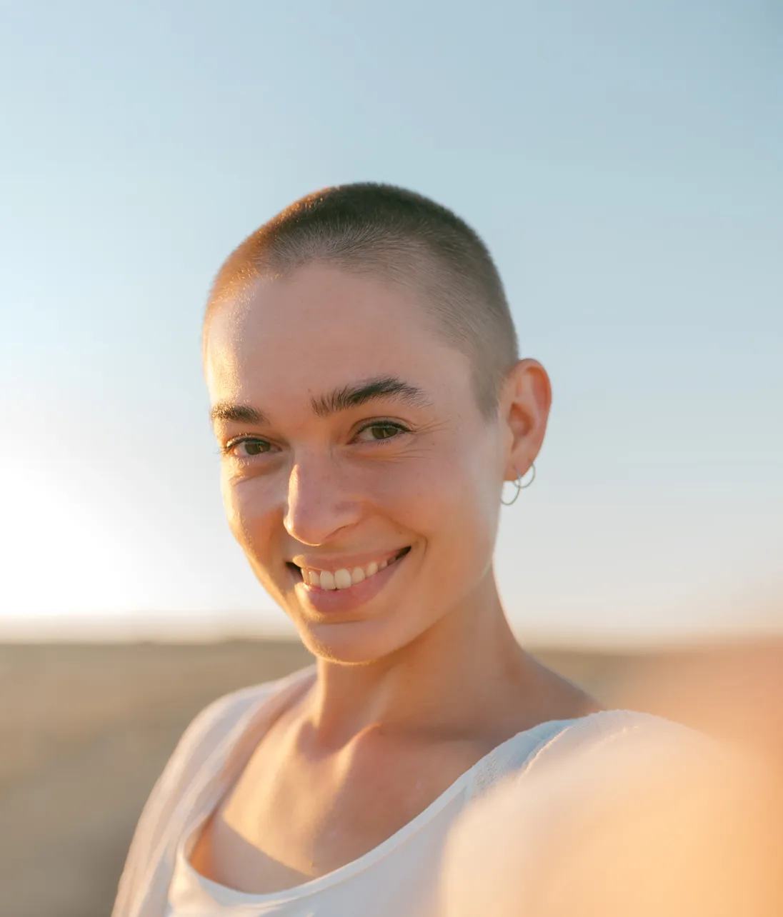 A young woman with a shaved head smiling directly at the camera