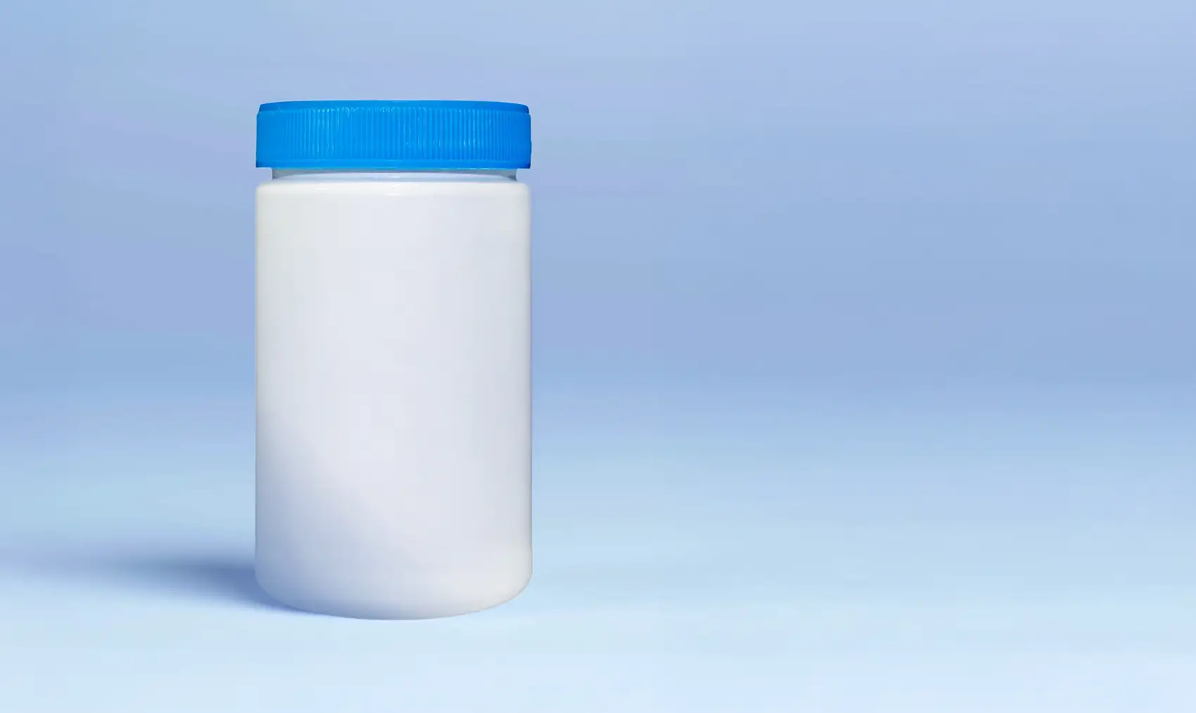 Plain white plastic jar with a blue lid on a light blue background. Plain white plastic jar with a blue lid on a light blue background.