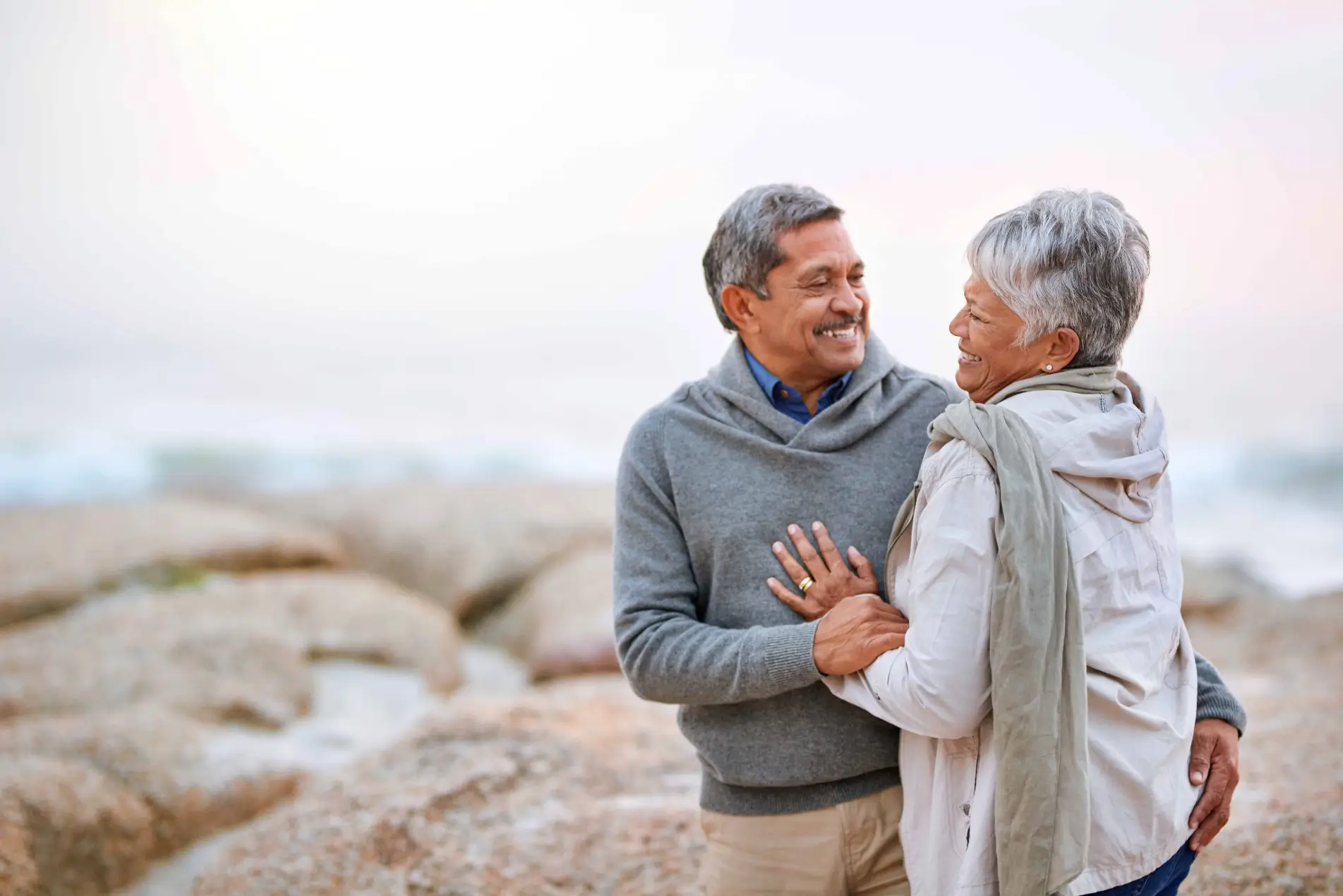 Smiling senior couple embracing on a rocky beach.
