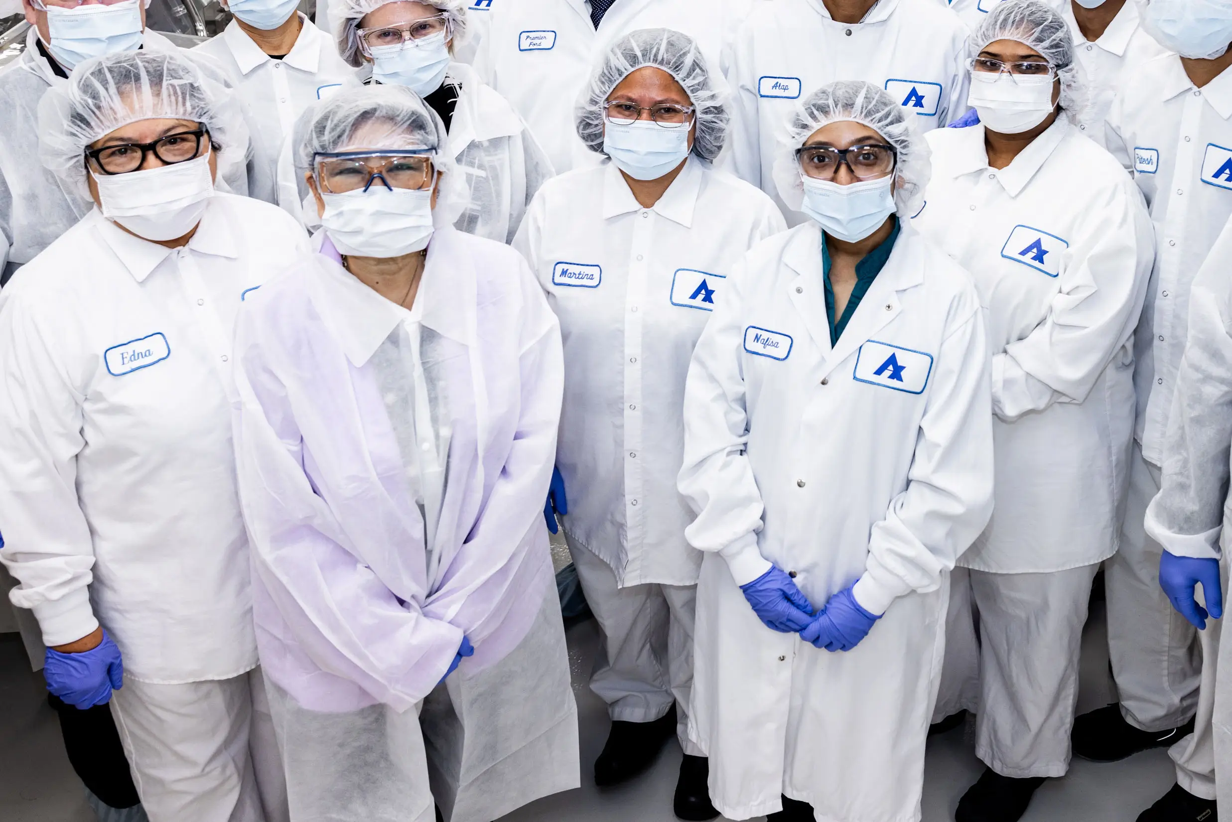 Empleados de fabricación de pie juntos con uniforme de laboratorio frente a la cámara