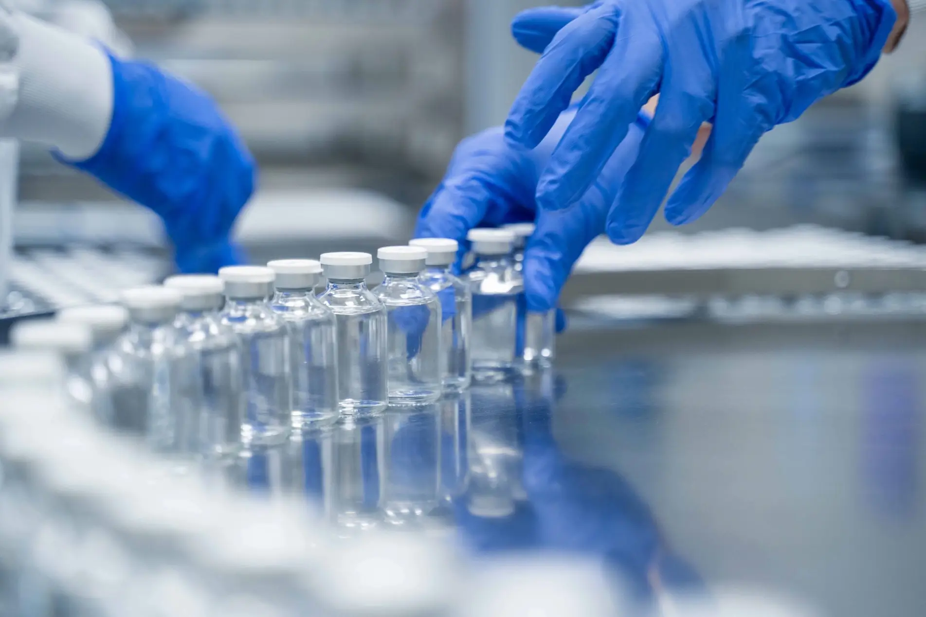 Hands in blue gloves handling medicine vials.